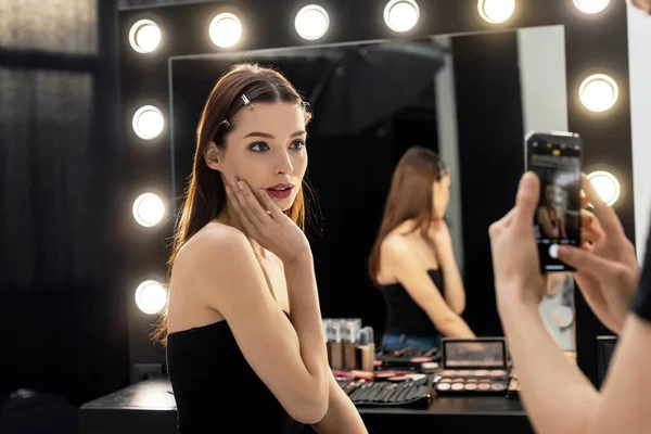 Enfoque selectivo de artista de maquillaje tomar fotos de modelo hermoso mientras se utiliza el teléfono inteligente - foto de stock