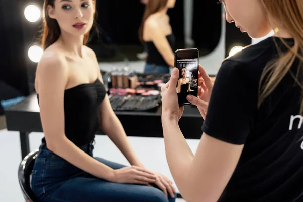 Selective focus of makeup artist taking photo of young model — Stock Photo