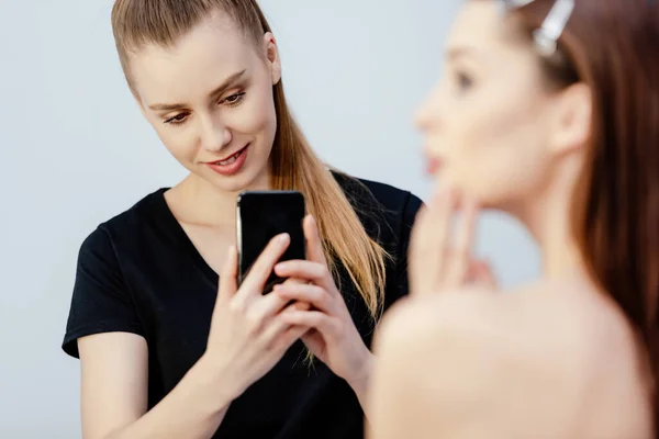 Selective focus of happy makeup artist taking photo of young model isolated on white — Stock Photo