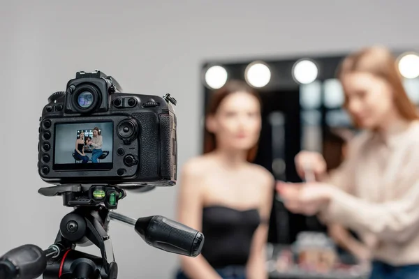 Selective focus of digital camera with makeup artist holding lip gloss near model on screen isolated on grey — Stock Photo