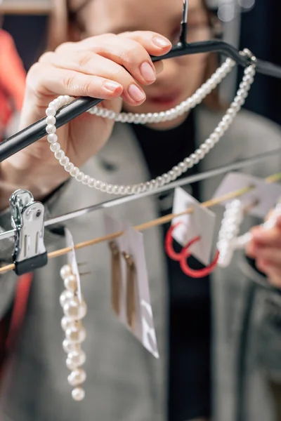 Enfoque selectivo de estilista tocando collar de perlas cerca de pendientes - foto de stock