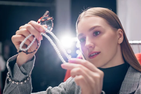 Selective focus of beautiful stylist looking at pearl necklace — Stock Photo