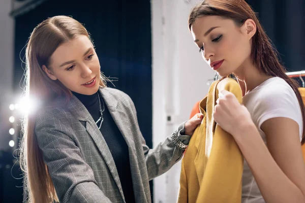 Attractive stylist holding yellow jacket near model — Stock Photo