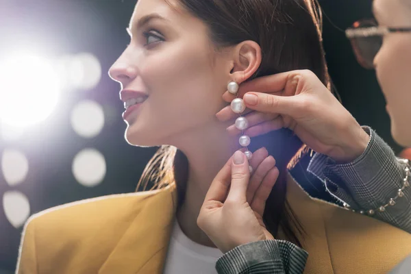 Selective focus of stylist in glasses touching earring on happy model — Stock Photo