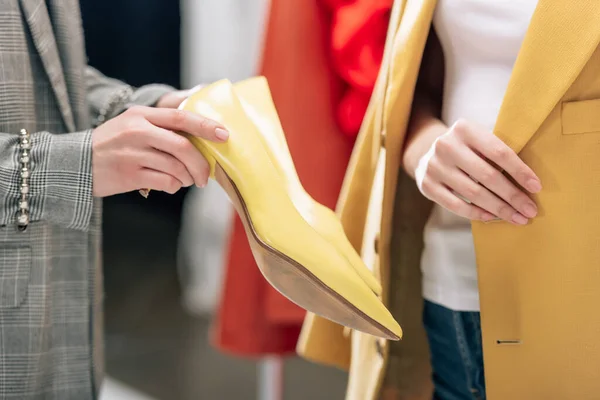 Vue recadrée du styliste tenant des chaussures jaunes près du modèle dans le studio photo — Photo de stock