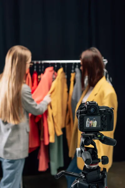 Foco seletivo da câmera digital com estilista tocando roupas na moda perto do modelo na tela — Fotografia de Stock