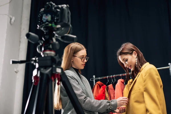Fuoco selettivo di stilista in occhiali che toccano giacca su modello felice vicino a macchina fotografica digitale — Foto stock