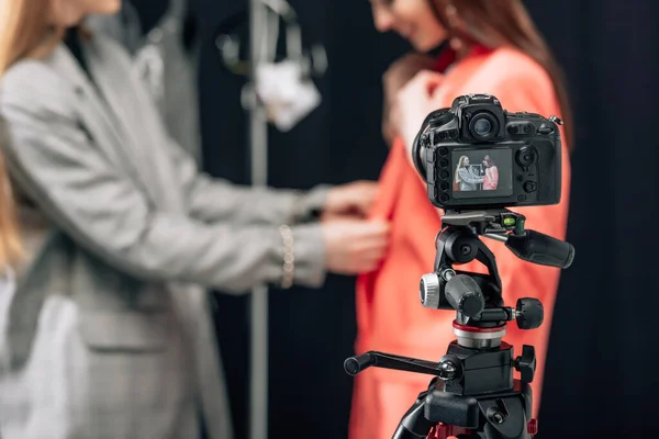Selective focus of digital camera with happy stylist touching jacket on model — Stock Photo