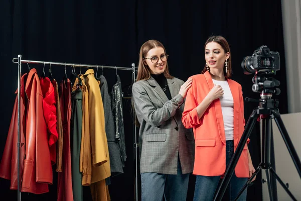 Enfoque selectivo de estilista en gafas tocando chaqueta de moda en modelo atractivo cerca de la cámara digital - foto de stock