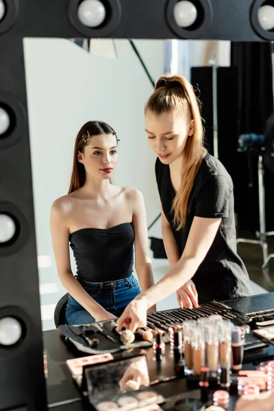 Selective focus of make up artist touching cosmetic brushes near model — Stock Photo