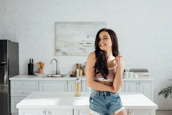 Mujer con los ojos cerrados sonriendo cerca de la mesa en la cocina - foto de stock