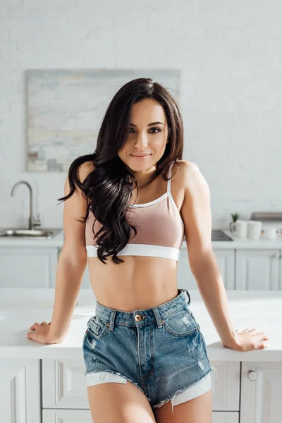 Mulher sorrindo e olhando para a câmera perto da mesa na cozinha — Fotografia de Stock