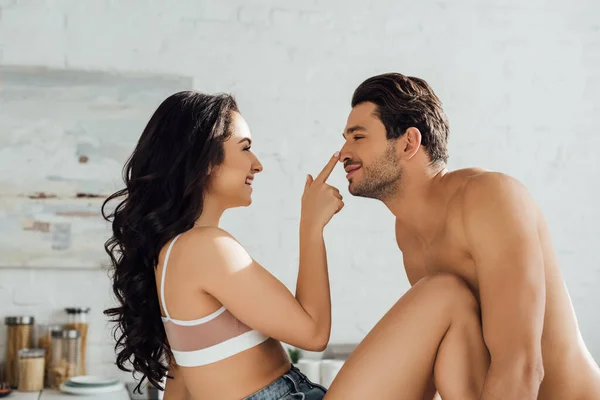 Pareja sonriendo, mirándose y chica tocando la nariz masculina en la cocina - foto de stock