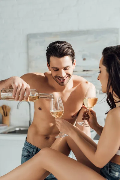 Man smiling and pouring wine in glasses in female hands in kitchen — Stock Photo