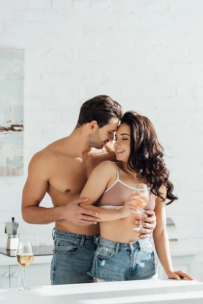 Hombre abrazando chica con vaso de vino por detrás en la cocina - foto de stock