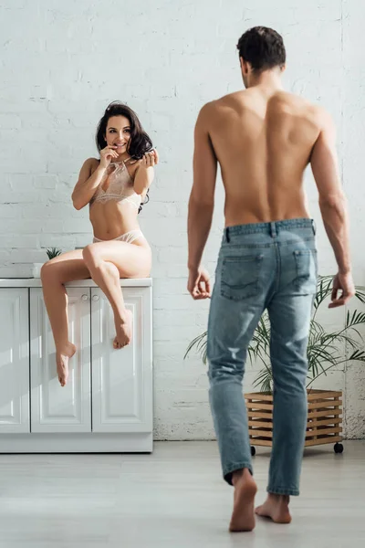 Femme sexy souriante, assise sur une armoire de cuisine et regardant son petit ami — Photo de stock