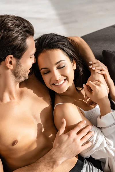 Visão de alto ângulo do homem abraçando namorada feliz com olhos fechados no sofá — Fotografia de Stock