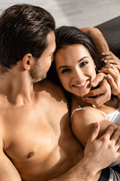Високий кут зору чоловіка обіймає щасливу і сексуальну дівчину, дивлячись на камеру на дивані — стокове фото