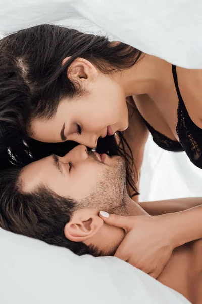 Paar umarmt und lächelt mit geschlossenen Augen unter Bettlaken im Schlafzimmer — Stockfoto