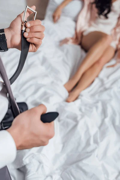 Cropped view of businessman unfastening belt in front of woman lying on bed in bedroom — Stock Photo