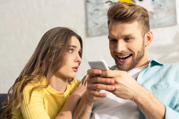 Foco seletivo da mulher olhando para namorado alegre com smartphone — Fotografia de Stock