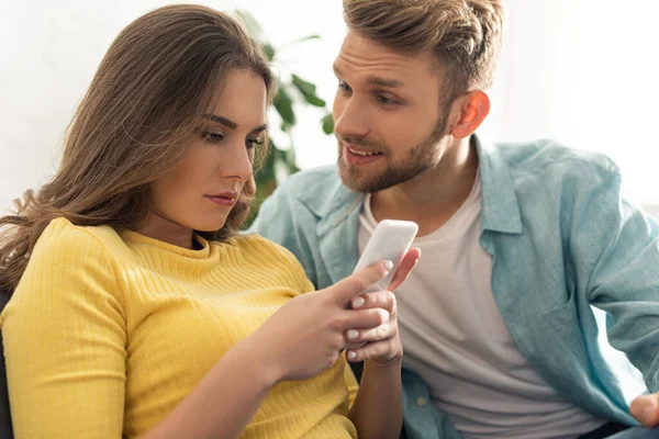 Focus sélectif d'un homme souriant regardant sa petite amie en utilisant un smartphone — Photo de stock