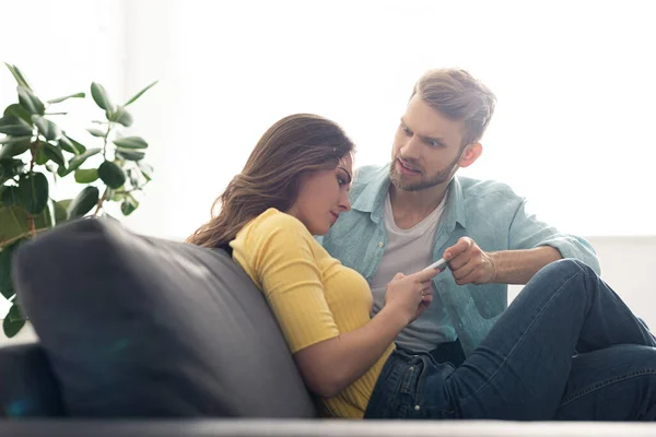 Selective focus of angry man taking smartphone from depended girlfriend — Stock Photo