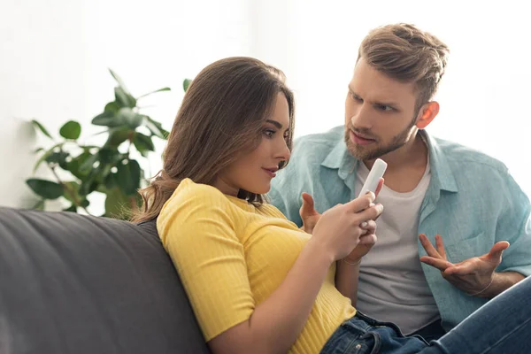 Depended woman using smartphone near angry boyfriend on couch — Stock Photo