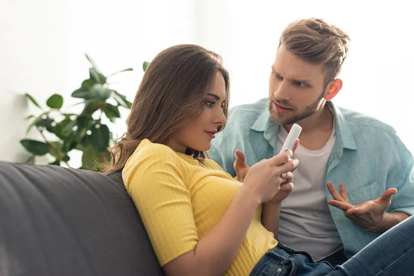 Abhängige Frau nutzt Smartphone neben wütendem Freund auf Couch — Stockfoto