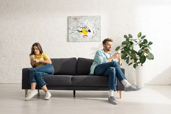 Casal jovem usando smartphones no sofá em casa — Fotografia de Stock