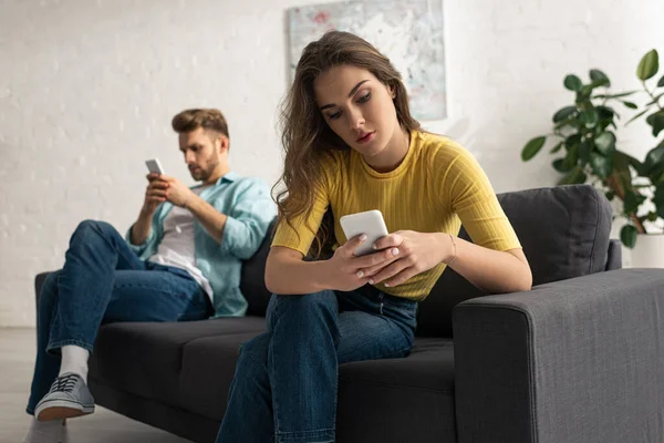 Foco seletivo da mulher usando smartphone perto do namorado no sofá — Fotografia de Stock