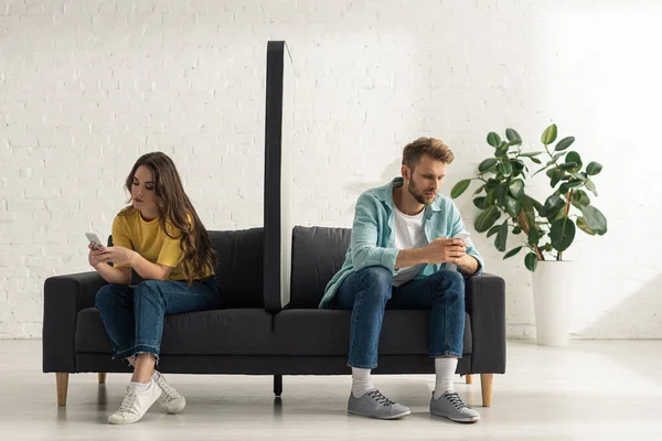 Model of smartphone on couch between young couple using smartphones in living room — Stock Photo