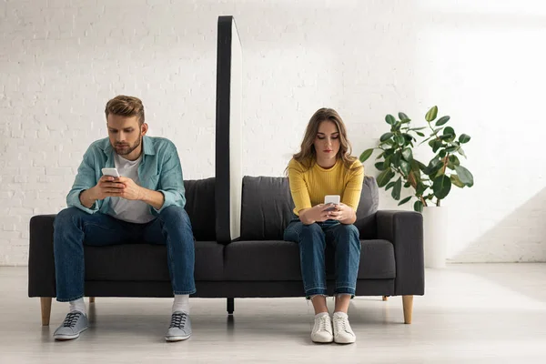 Young couple using smartphones near big model of smartphone on couch at home — Stock Photo