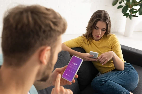 KYIV, UKRAINE - FEBRUARY 21, 2020: Selective focus of man using smartphone with instagram app near girlfriend on sofa — Stock Photo