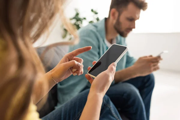 Selective focus of woman holding smartphone with blank screen near boyfriend on sofa — Stock Photo