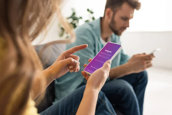 KYIV, UKRAINE - FEBRUARY 21, 2020: Selective focus of woman pointing with finger at smartphone with instagram app near boyfriend on couch — Stock Photo