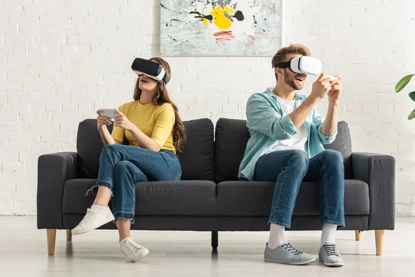 Couple utilisant des écouteurs de réalité virtuelle et smartphones sur le canapé — Photo de stock