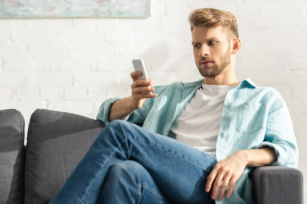 Selective focus of handsome man using smartphone on couch — Stock Photo