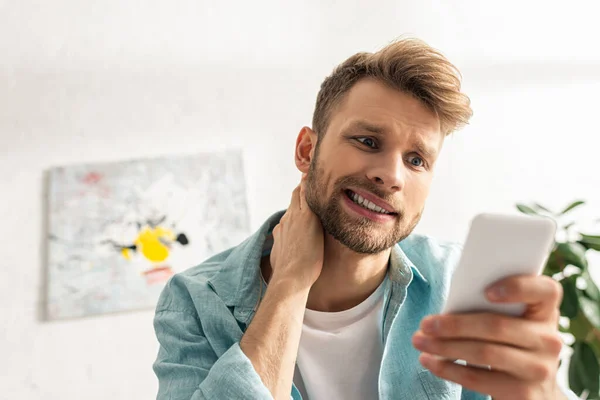 Focus selettivo dell'uomo confuso che guarda lo smartphone in salotto — Foto stock