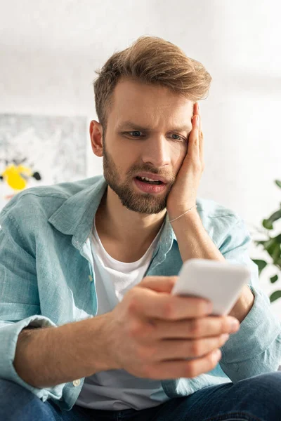 Selective focus of worried man using smartphone at home — Stock Photo