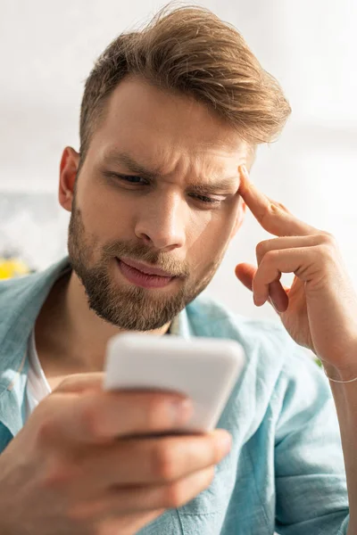 Selective focus of thoughtful man with fingers near forehead using smartphone — Stock Photo