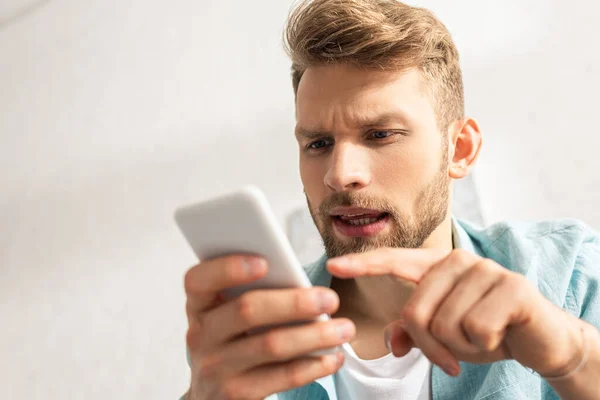 Selective focus of handsome man pointing with finger at smartphone — Stock Photo