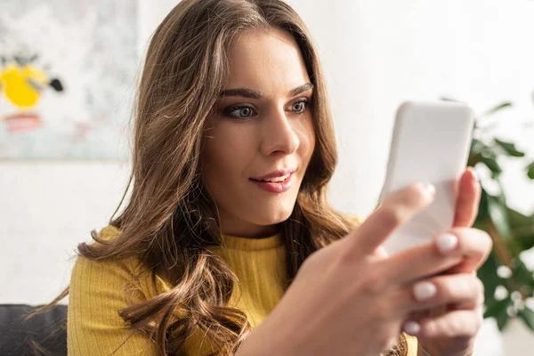 Foco seletivo de sorrir dependia mulher usando smartphone no sofá — Fotografia de Stock