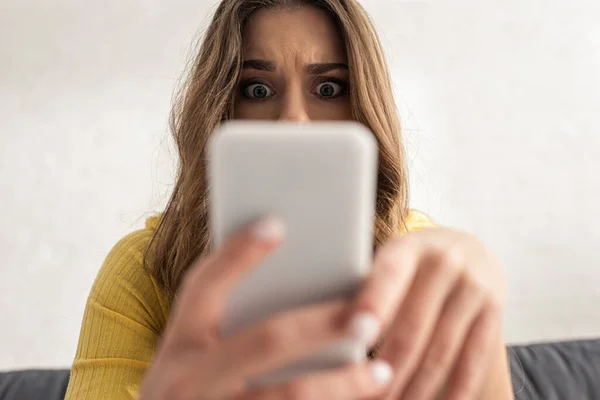 Selective focus of shocked girl using smartphone at home — Stock Photo