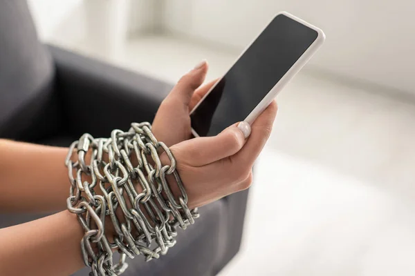 Vista cortada da mulher com corrente de metal em torno de mãos segurando smartphone com tela em branco no sofá — Fotografia de Stock