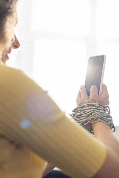 Selective focus of young woman holding smartphone in tied hands with metal chain — Stock Photo