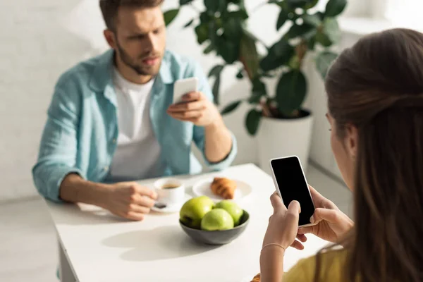 Enfoque selectivo de la mujer usando teléfono inteligente cerca de novio charlando durante el desayuno - foto de stock