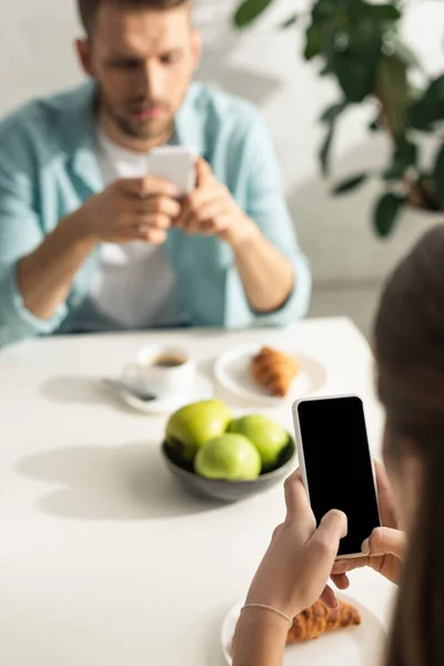 Enfoque selectivo de la mujer usando smartphone con pantalla en blanco durante el desayuno con el novio - foto de stock