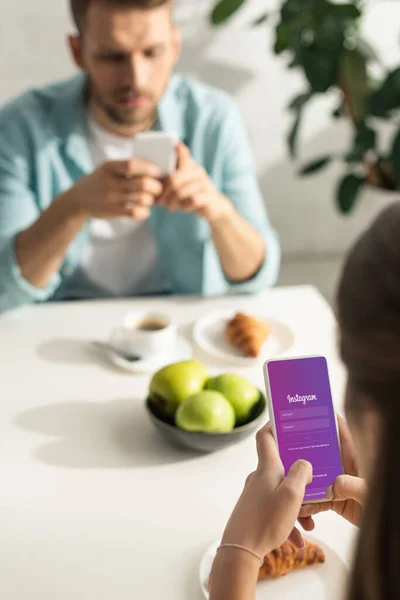 KYIV, UCRANIA - 21 DE FEBRERO DE 2020: Enfoque selectivo de la mujer usando la aplicación instagram durante el desayuno con el hombre - foto de stock