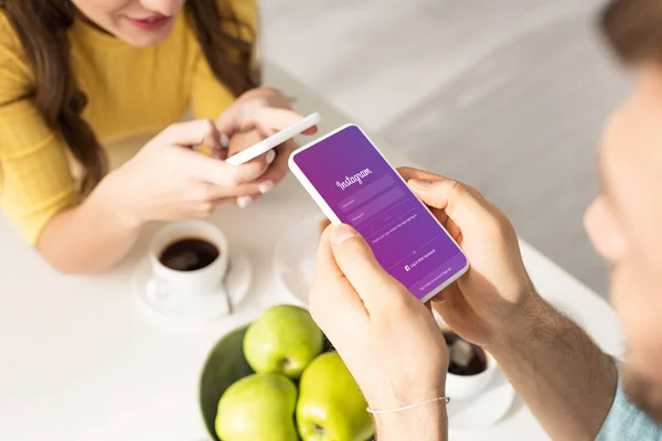 KYIV, UKRAINE - FEBRUARY 21, 2020: Selective focus of man using smartphone with instagram app near girlfriend during breakfast in kitchen — Stock Photo